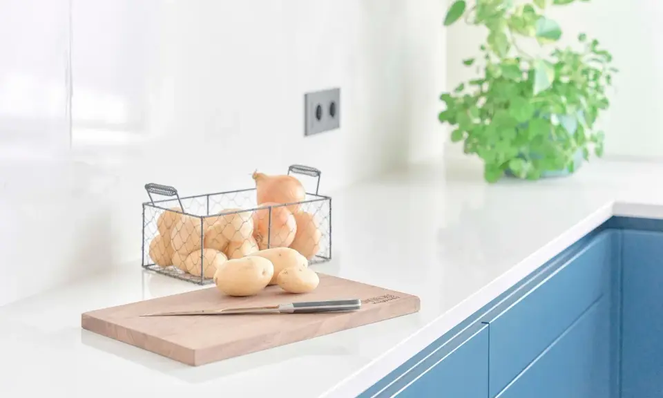 Encimeras de cocina blancas y lisas, con patatas y cebollas listas para cocinar.