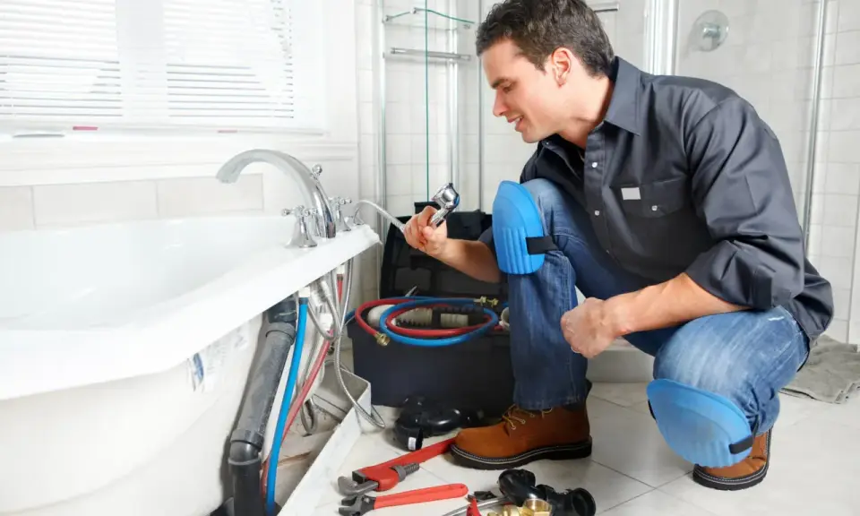 Plombier vérifiant la pose de la baignoire, outils et tuyaux à proximité.