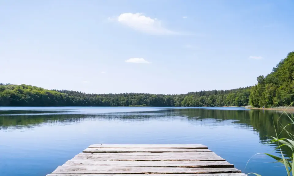 Holzsteg am ruhigen See, umgeben von grünen Wäldern. Ein perfekter Ort für einen geheimtipp mecklenburgische seenplatte Urlaub.