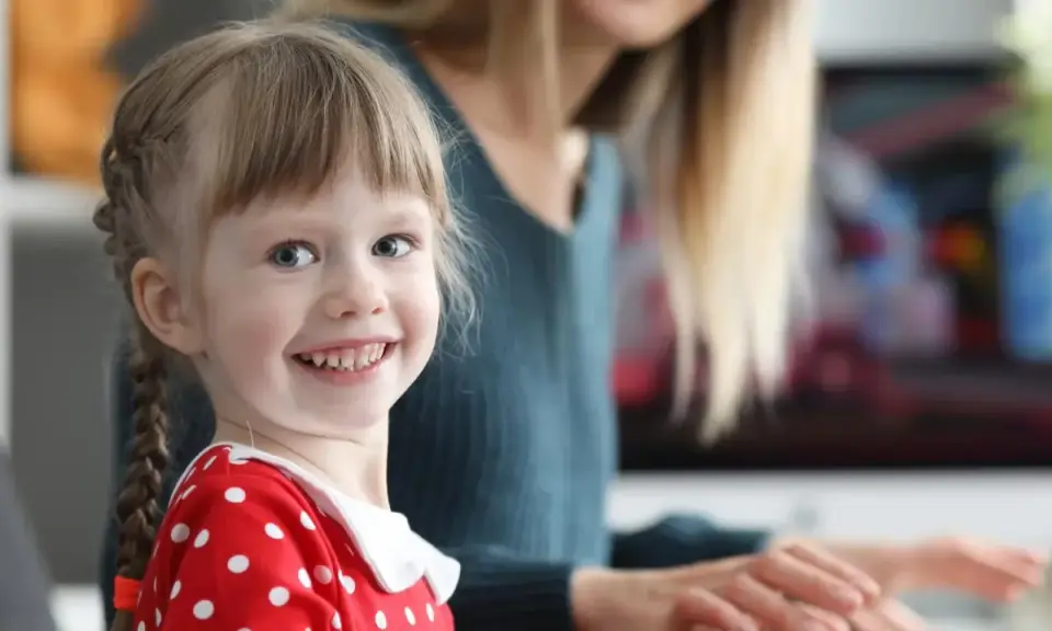 Uśmiechnięta dziewczynka w czerwonej sukience w groszki, z warkoczykami, uczy się kindersztuby od mamy.