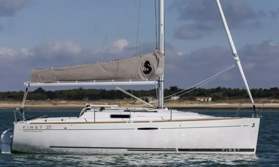 Voilier blanc "First 25 Performance" naviguant sur une mer calme, avec une voile grise arborant un logo noir.
