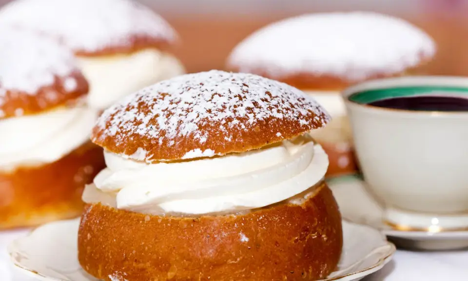 Semlor, en fest vid fastan, pudrade med florsocker och fyllda med grädde. En kopp kaffe i bakgrunden.