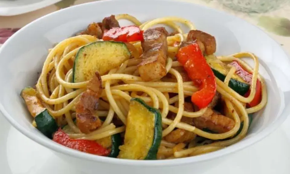 Un plato de espaguetis con pimientos rojos y calabacín salteados, con trozos de carne.