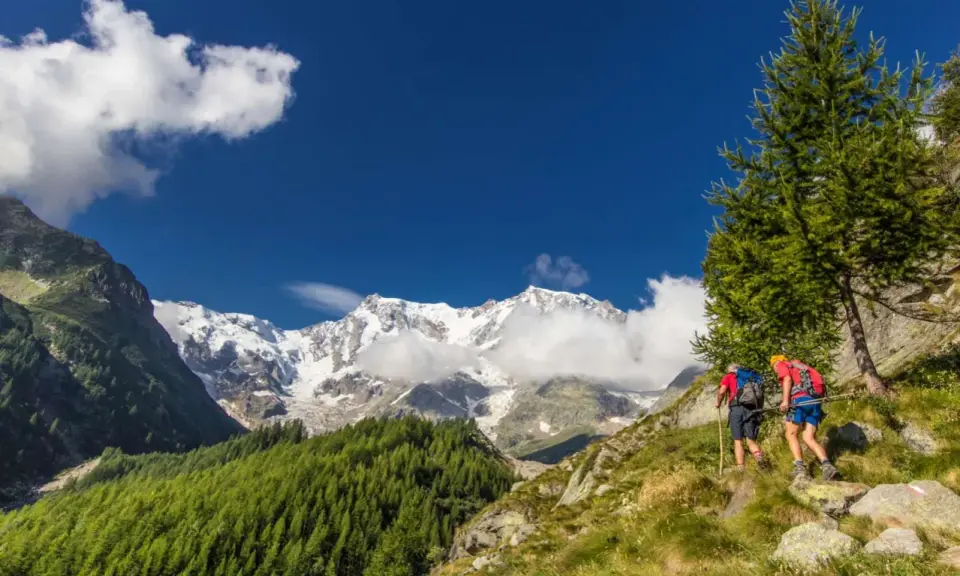Due escursionisti affrontano un sentiero in Val d'Ossola, con maestose cime innevate sullo sfondo. Perfetto per escursioni facili.
