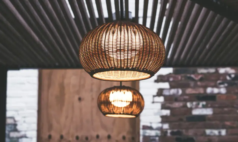 Dos lámparas de mimbre esféricas cuelgan bajo un techo de listones. La luz cálida que emiten crea un ambiente acogedor, con unos lumenes por m2 perfectos para relajarse.