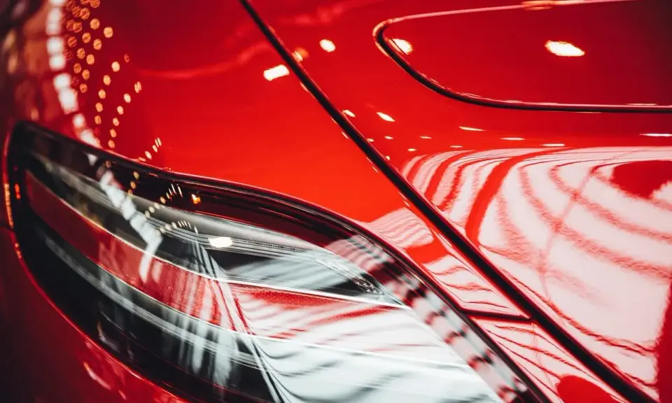 Błyszczący, czerwony lakier samochodu, odbijający światła. Widać fragment lampy. To praca detailera, który doprowadził auto do perfekcji.
