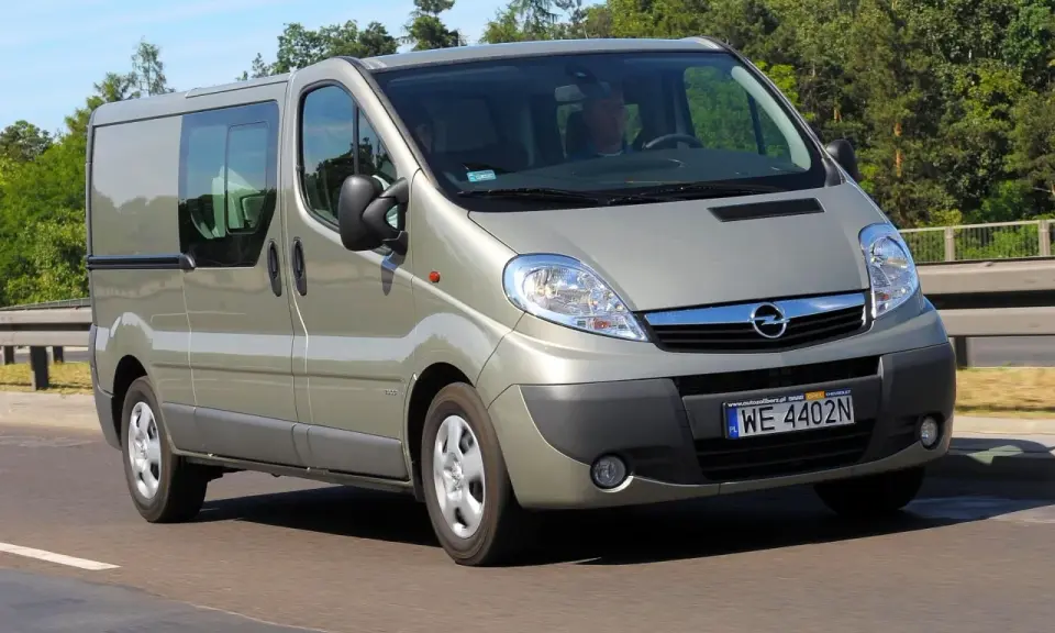 Srebrny Opel Vivaro 2.0 CDTI z przyciemnianymi szybami jedzie po drodze, otoczony zielenią.