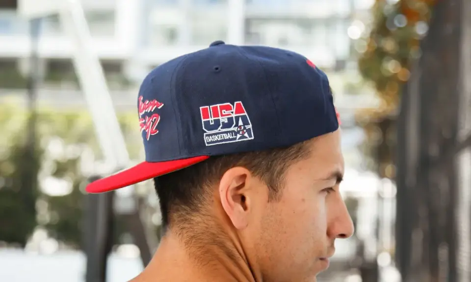 Junger Mann trägt eine dunkelblaue Kappe mit rotem Schirm und "USA Basketball"-Aufdruck, den **cap nach hinten tragen** ist sein Stil.