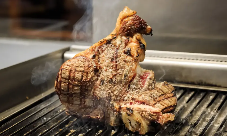 Una succulenta bistecca a Firenze, cotta alla perfezione sulla griglia, con sale grosso e fumo che sale.