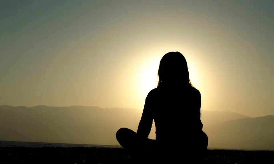 Silhuett av en person som mediterar vid solnedgången. Kanske är det en av nackdelar med meditation att man blir så fokuserad att man missar allt annat.