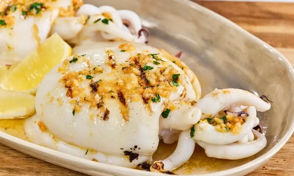 Delicioso sepia a la plancha con ajo, perejil y limón, servido en una bandeja.