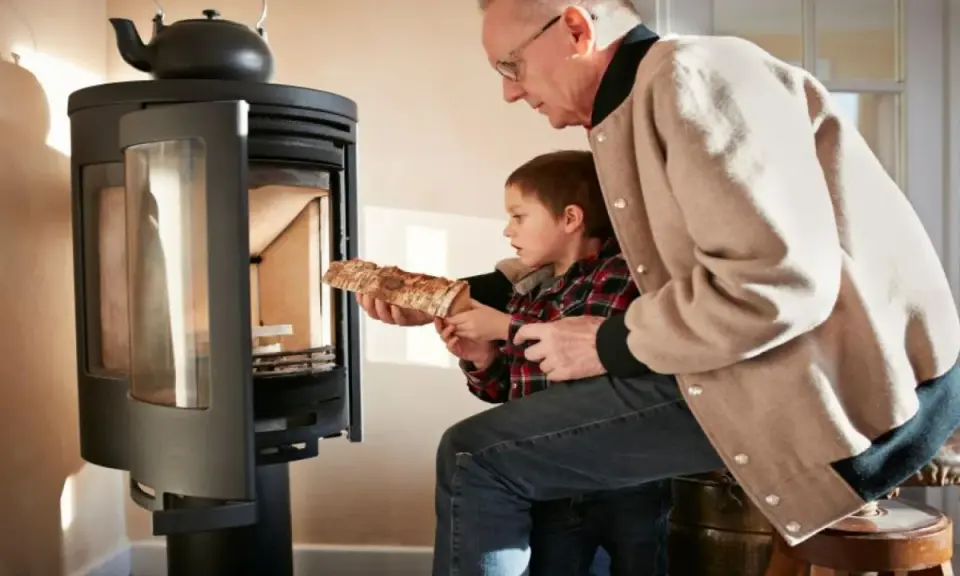 Un grand-père aide son petit-fils à charger du bois dans un poêle. Une alternative au chauffage au fioul, mais attention aux dangers du feu.