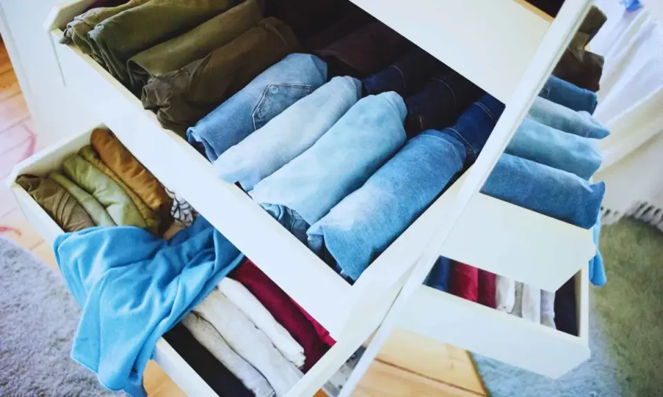 Cajones de armario organizados tras una **limpieza de armario**. Ropa doblada y ordenada por color y tipo, predominan los vaqueros y prendas en tonos tierra y azules.