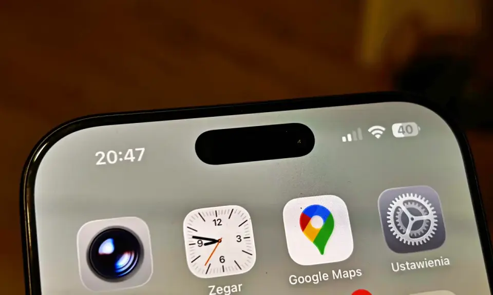 Ekran iPhone z widoczną dynamiczną wyspą, ikonami Aparat, Zegar, Google Maps i Ustawienia. Czas 20:47.
