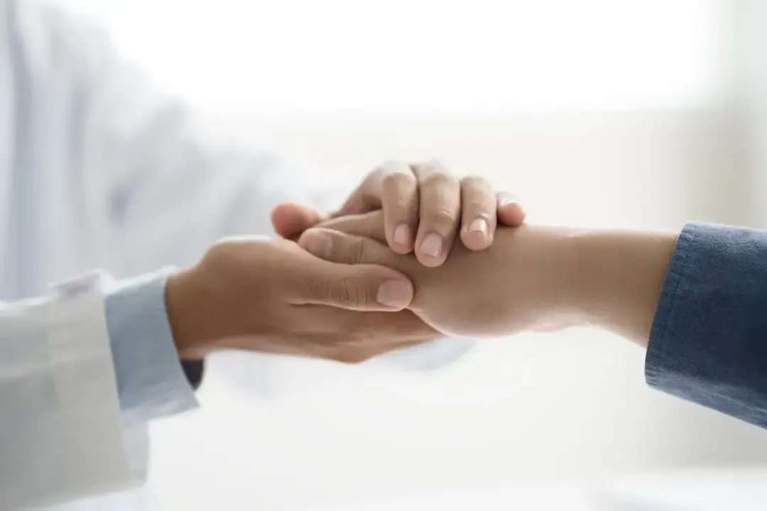 Dłoń lekarza w białym kitlu pociesza dłoń pacjenta. Symbol wsparcia i empatii, ważny dla osób z niepełnosprawnością.