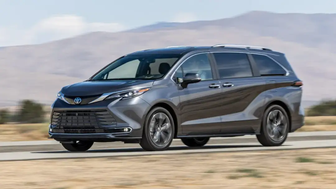 Szary minivan Toyota Sienna pędzi po pustynnej drodze, z górzystym krajobrazem w tle.