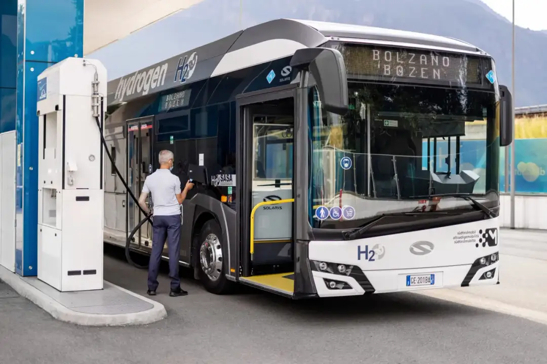 Mężczyzna tankuje autobus elektryczny na stacji wodorowej. Pojazd z napisem "Hydrogen H2" jest gotowy do dalszej podróży.
