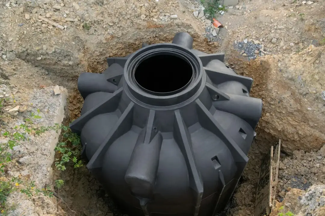 Czarny plastikowy szambo w wykopie ziemnym, gotowe do montażu.