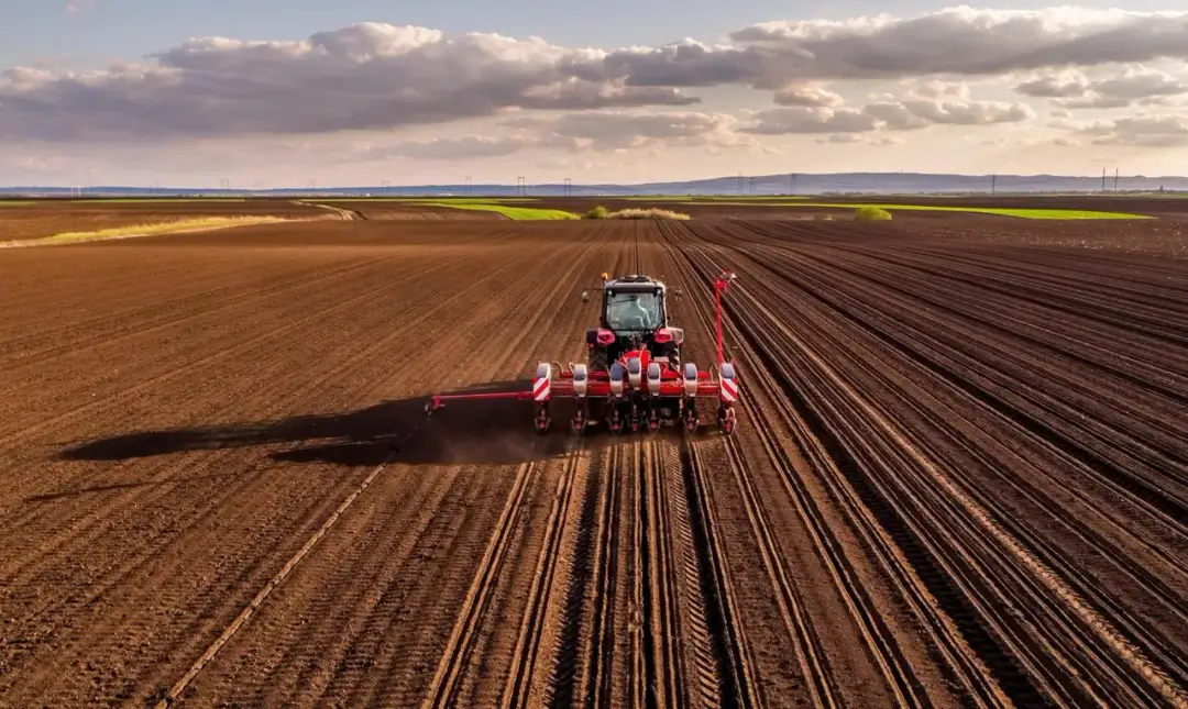 Czerwony traktor z siewnikiem na polu. Zastanawiasz się, ile kosztuje metr ziemi rolnej?