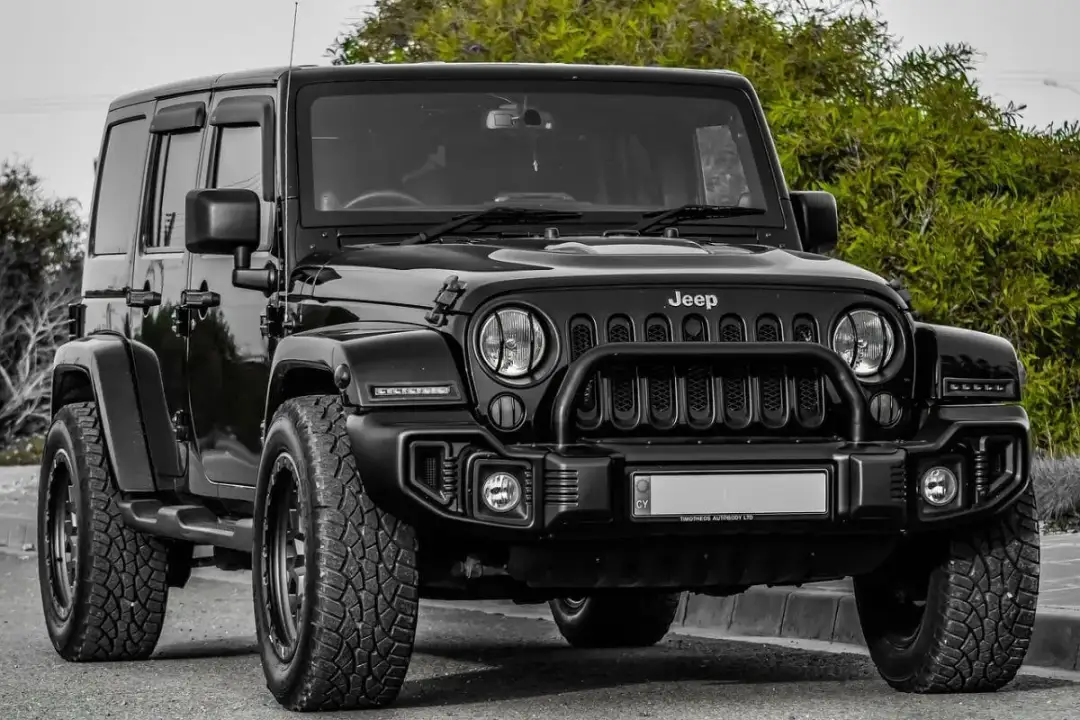 Czarny Jeep Wrangler, idealny SUV do 80 tys. zł, z terenowymi oponami i solidnym grillem, gotowy na przygodę.