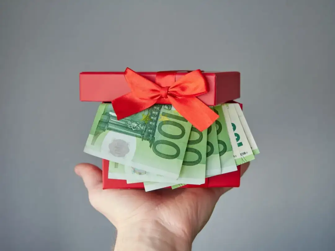 Czerwone pudełko z prezentem wypełnione banknotami euro, trzymane na dłoni.