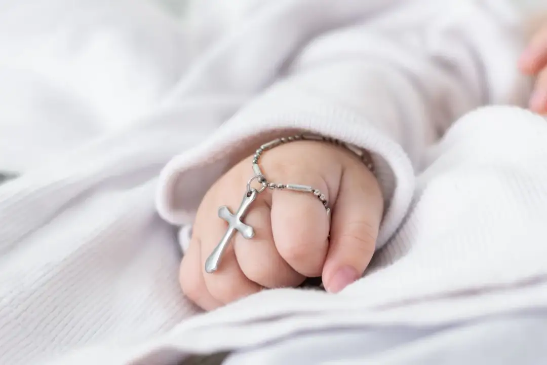 Dziecięca rączka z krzyżykiem na łańcuszku. Chrzestny na chrzciny często daje taki symboliczny prezent.