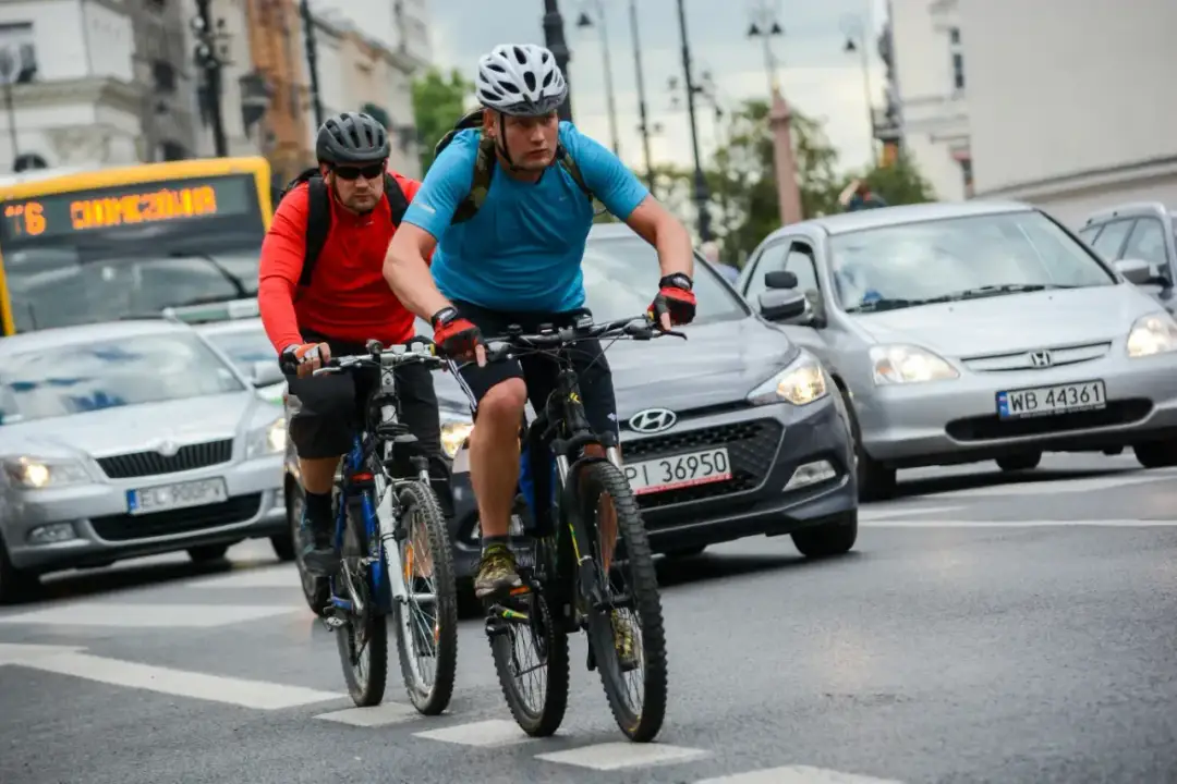 Dwóch rowerzystów w kaskach jedzie po ulicy, mijając samochody. Czy można jeździć rowerem po chodniku? Tutaj widać, że nie.