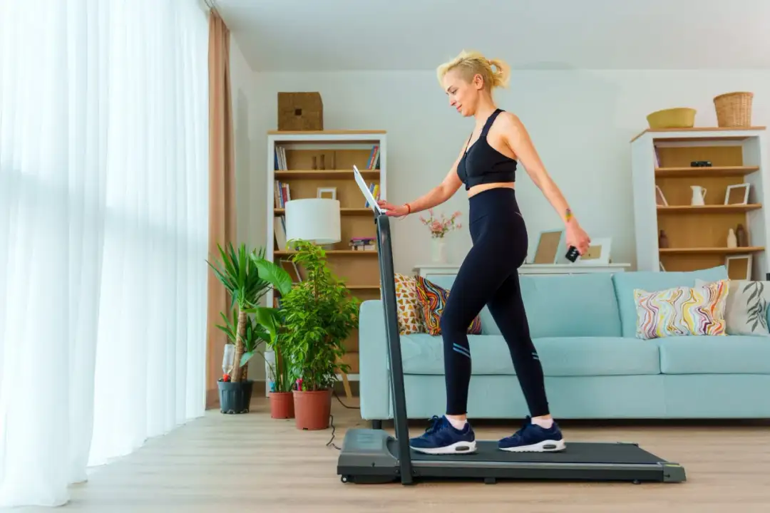 Kobieta w sportowym stroju ćwiczy na bieżni w domowym salonie.