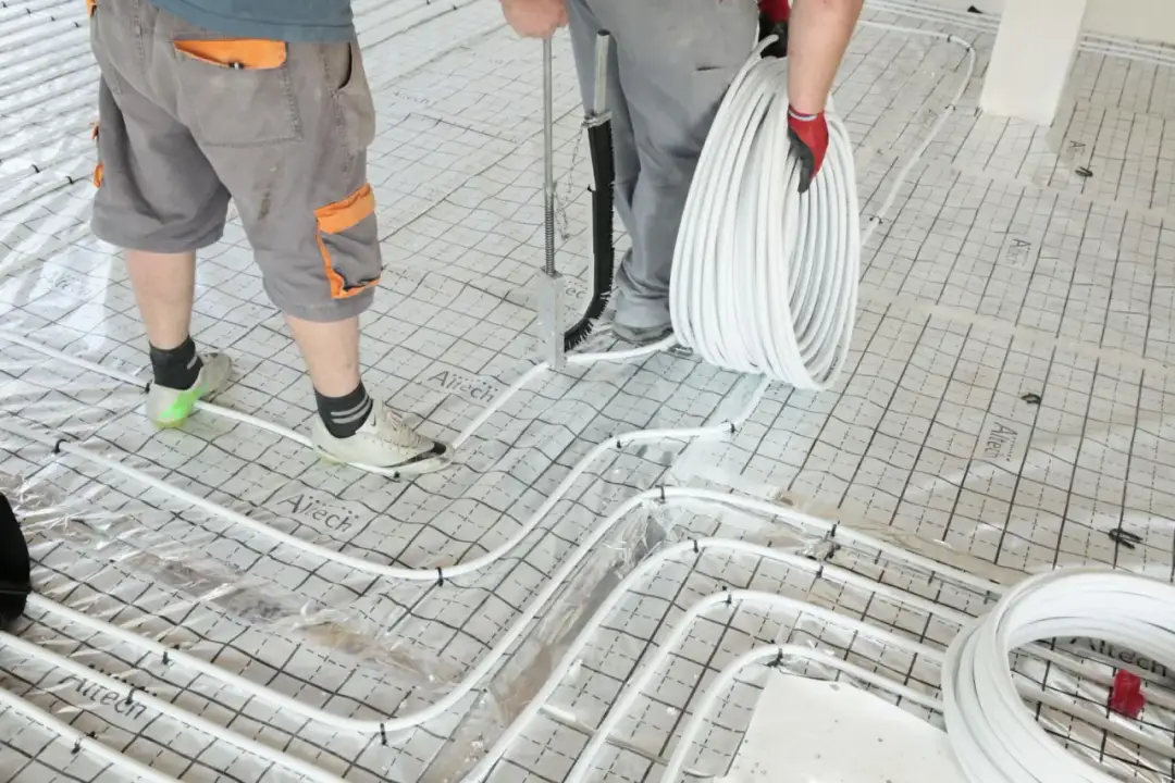 Pracownicy układają rury do ogrzewania podłogowego na siatce. Gotowa posadzka będzie ciepła i komfortowa.