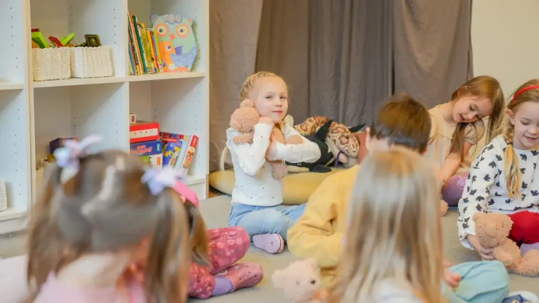 Dzieci siedzą na podłodze, słuchając bajki. To idealny moment, kiedy dziecko może iść do przedszkola.