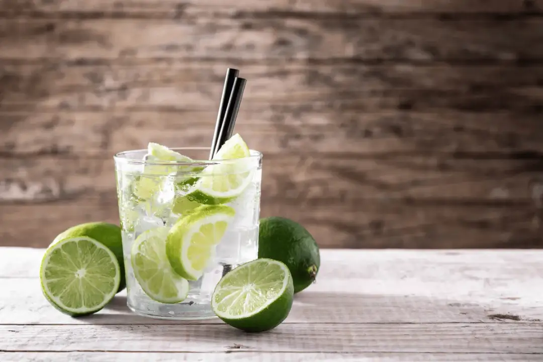 Orzeźwiający drink z limonką i lodem, otoczony świeżymi owocami. Idealny na upalne dni.