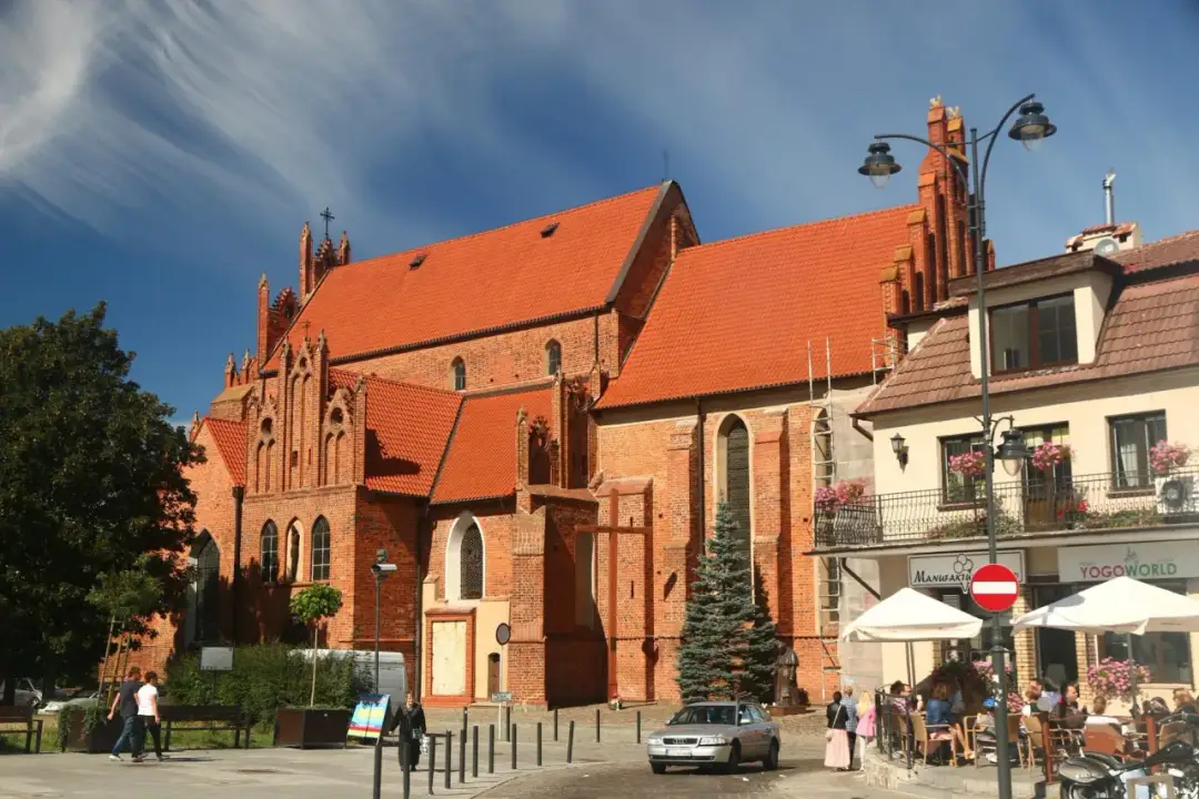 Gotycka ceglana bazylika z czerwonym dachem i błękitnym niebem.