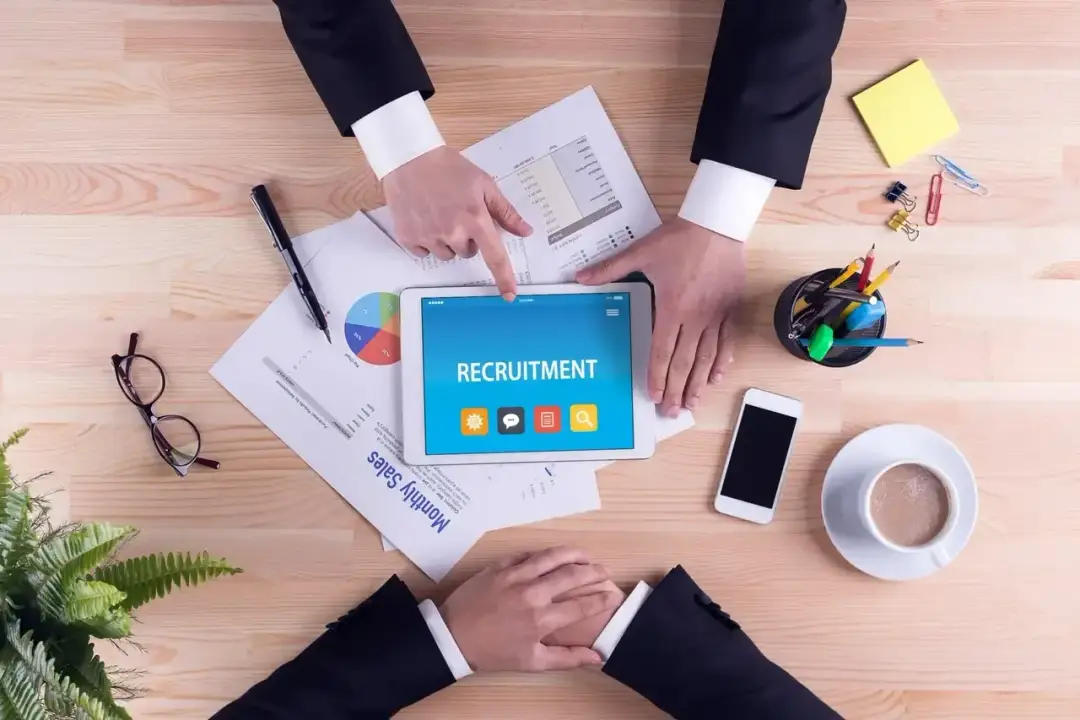 Rekrutacja ukryta: jak znaleźć oferty bez nazwy firmy? Na tablecie widnieje napis "RECRUITMENT", obok dokumenty i akcesoria biurowe.