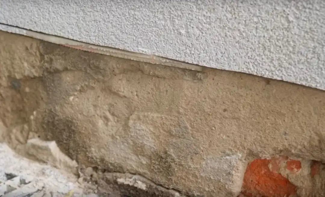 Fragment ściany z widocznym pęknięciem, przygotowanym do iniekcji. Widać warstwę tynku i ceglane podłoże.