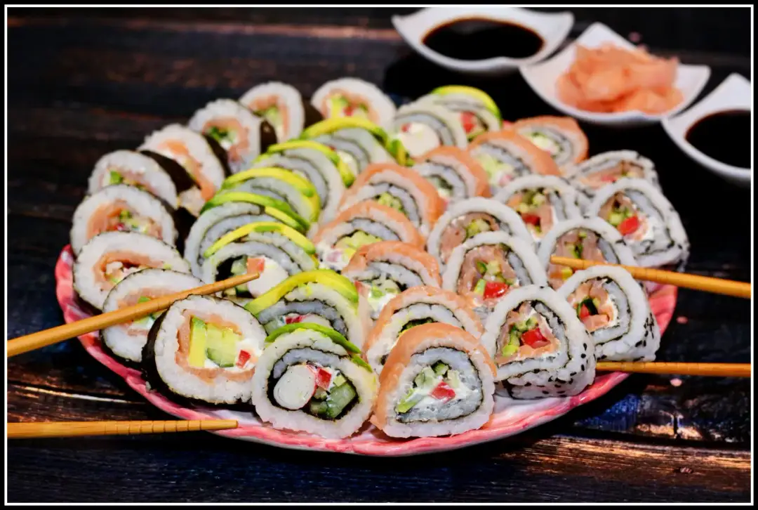 Talerz pełen kolorowych uramaki z łososiem, awokado i warzywami. Patyczki do sushi czekają na pierwszy kęs.