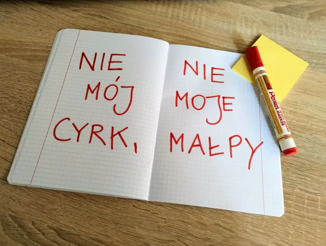 Otwarty zeszyt z zapisanymi czerwonym markerem polskimi idiomami: "Nie mój cyrk, moje małpy".