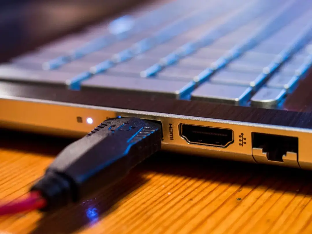 Wtyczka HDMI podłączona do laptopa, obok klawiatury.
