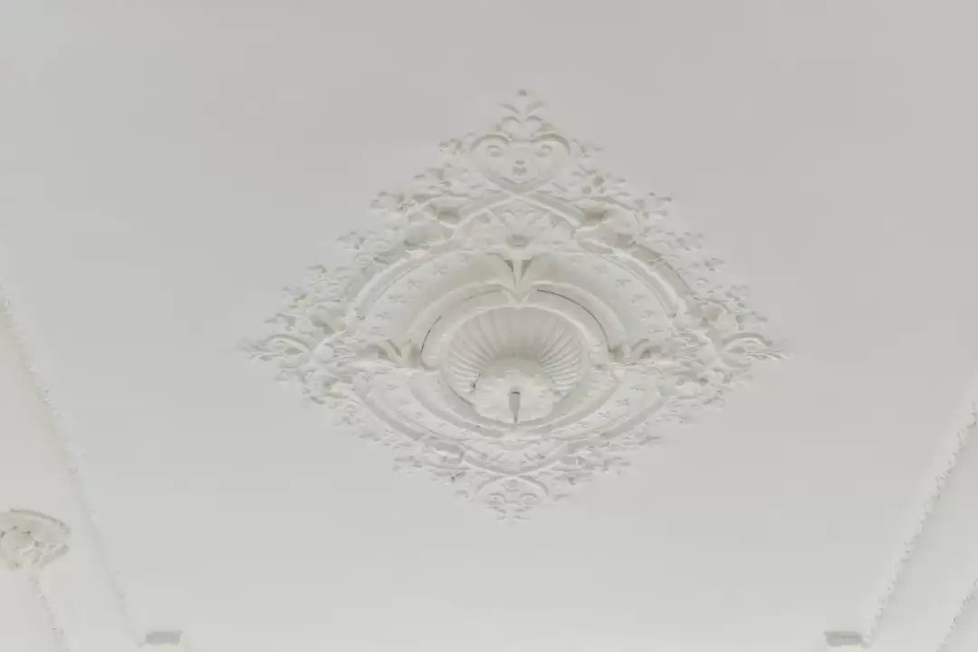 Elegancka, biała rozeta na suficie, ozdobiona misternymi wzorami roślinnymi i geometrycznymi.