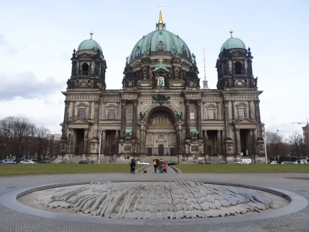 Majestatyczna katedra w Berlinie z zielonymi kopułami, na pierwszym planie kamienna rzeźba.