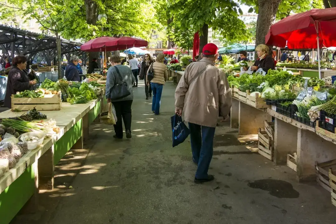 Ludzie spacerują między straganami z warzywami na targu.