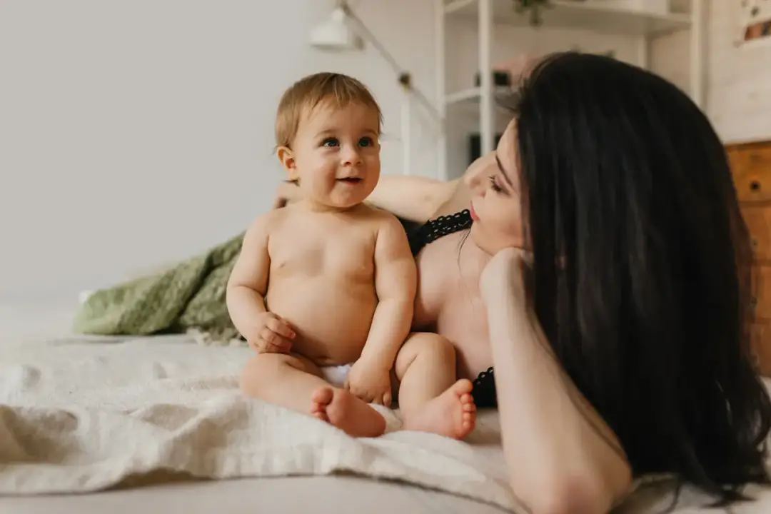 Uśmiechnięty niemowlak siedzi obok mamy. Zastanawiamy się, ile rośnie noworodek, obserwując jego rozwój.