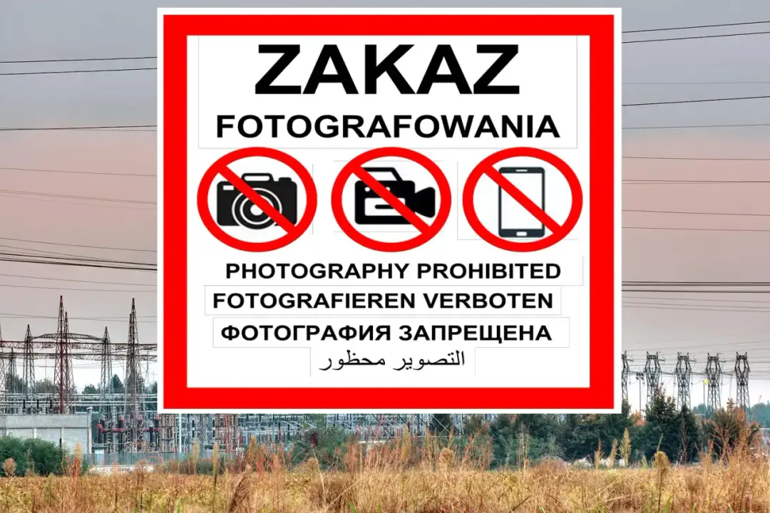 Znak ZAKAZ FOTOGRAFOWANIA na tle linii energetycznych i stacji transformatorowej.