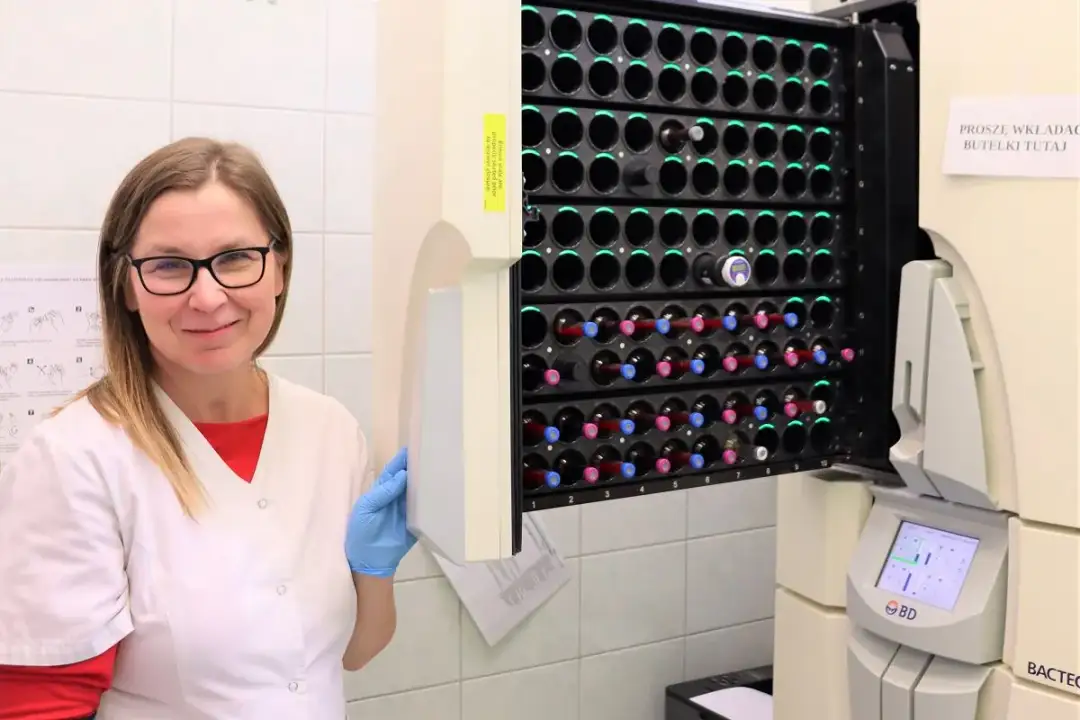 Uśmiechnięta laborantka w niebieskich rękawiczkach obok urządzenia do analizy próbek. To przyszłość po mikrobiologii, gdzie precyzja spotyka się z technologią.