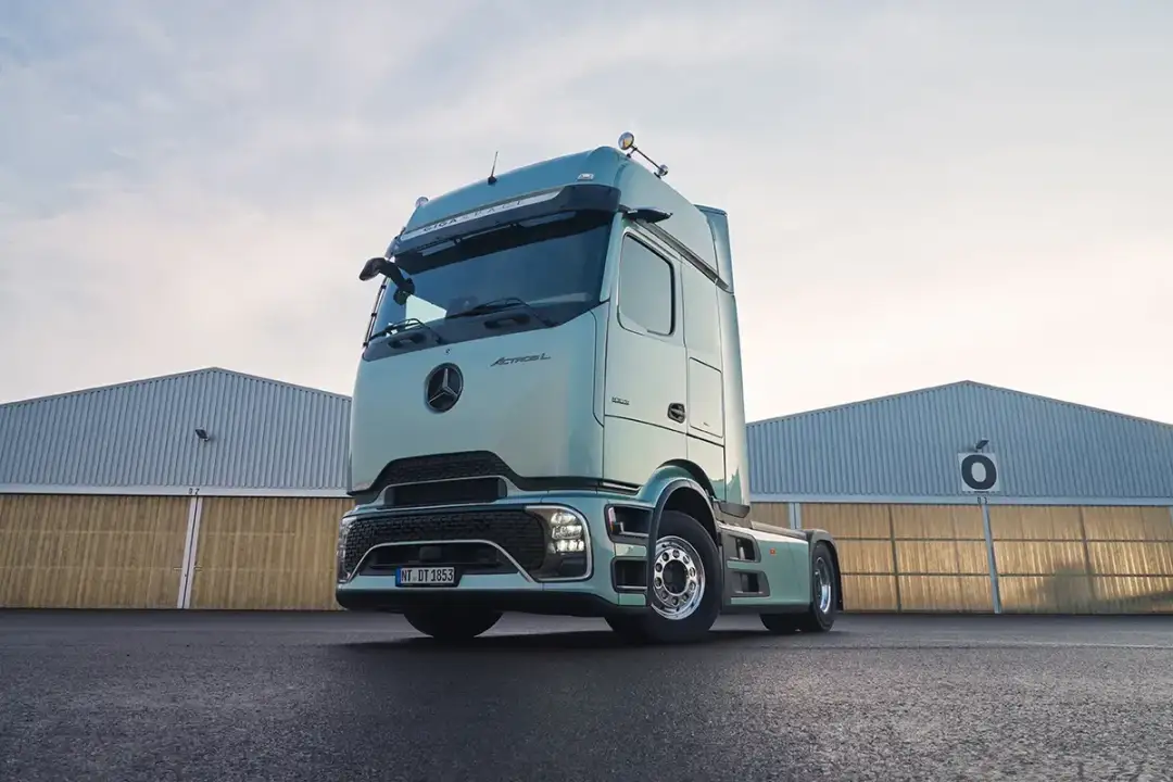 Nowy Mercedes Actros MP4 w kolorze miętowym, zaparkowany przed halami magazynowymi.