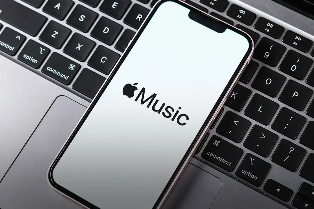 Telefon z logo Apple Music leży na klawiaturze laptopa. Sprawdź aktualną apple music cena.