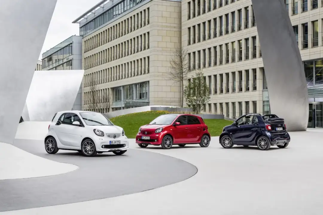 Trzy samochody Smart, w tym jeden w wersji Brabus, zaparkowane przed nowoczesnym budynkiem.