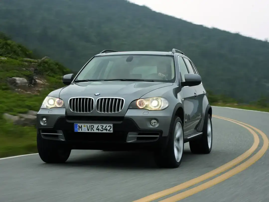 Szary BMW X5 E70 pokonuje zakręt na malowniczej górskiej drodze.