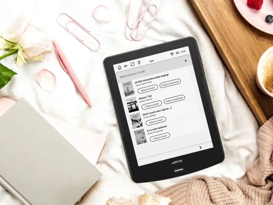 Czytnik ebooków z listą darmowych lektur i audiobooków, obok róż i filiżanka kawy.