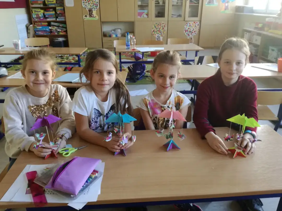 Cztery dziewczynki siedzą przy biurku i trzymają w rękach kolorowe origami.