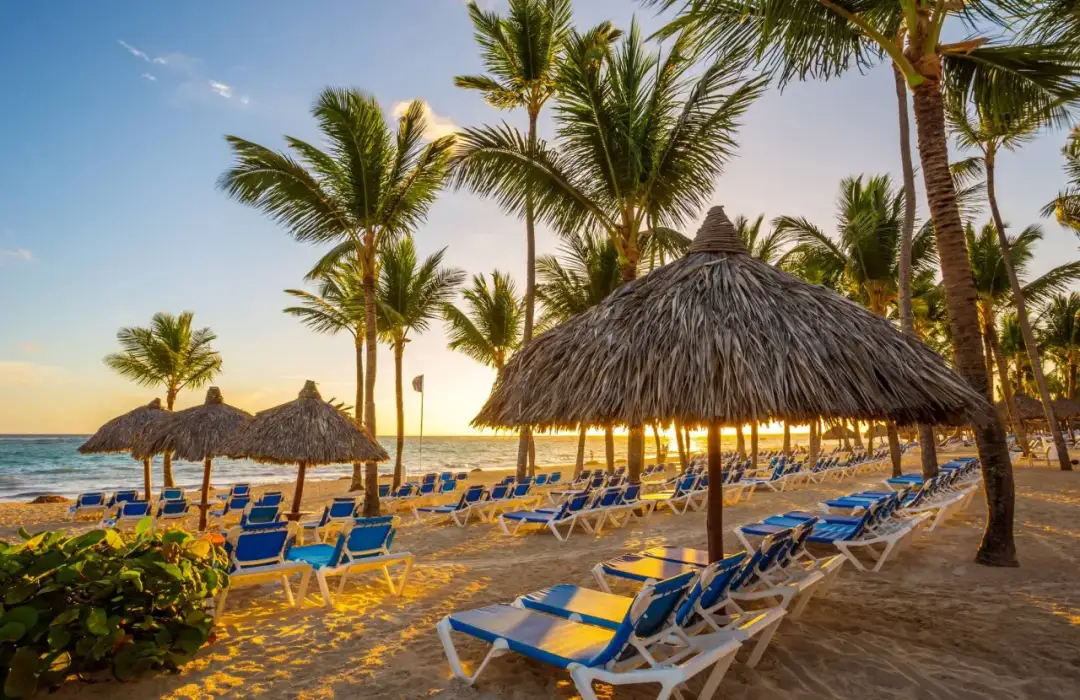Plaża w Punta Cana, Dominikana, z rzędami leżaków i palm. Słońce zachodzi, tworząc złote światło.
